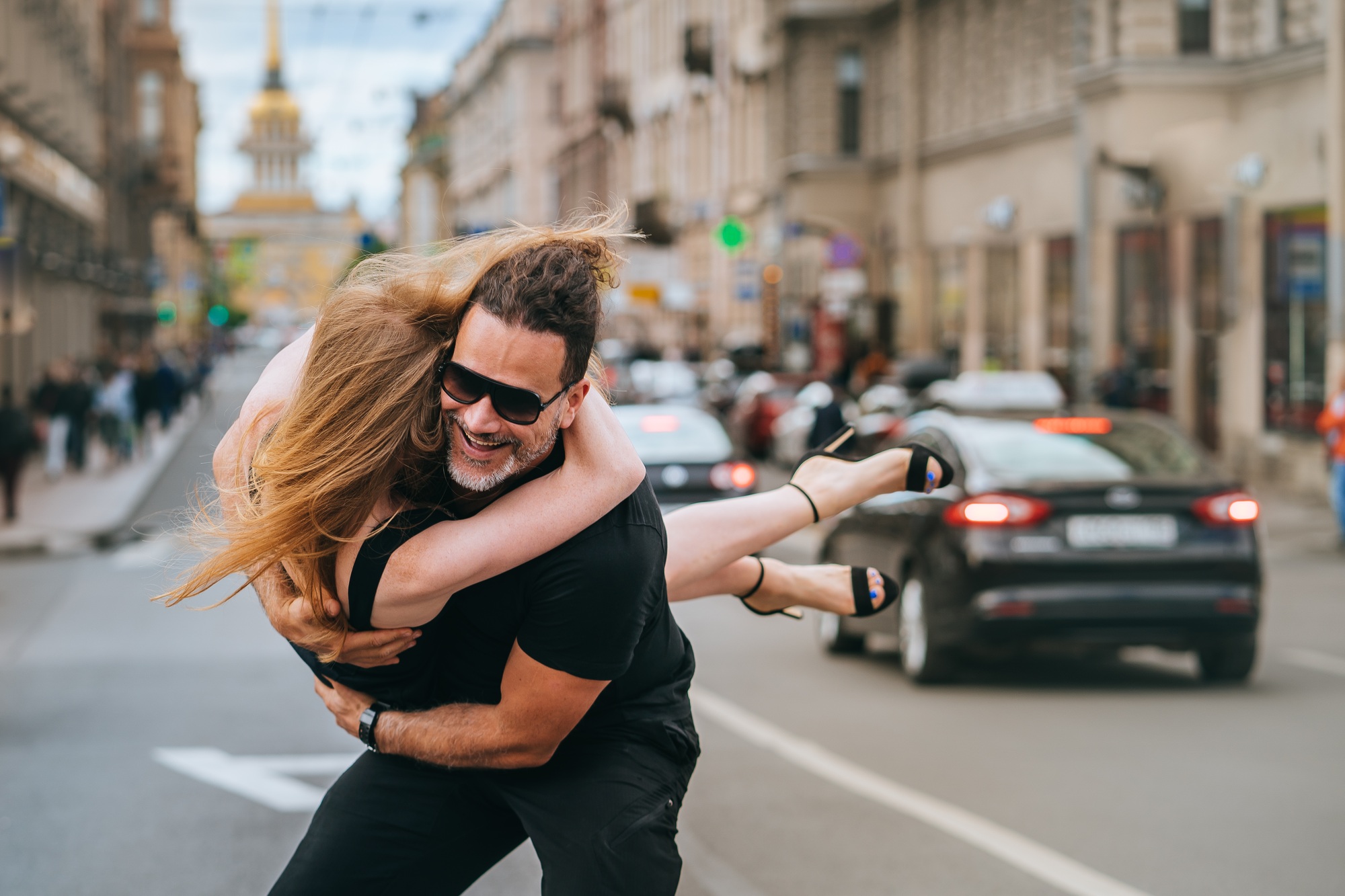 Excited strong Spanish man lifts up redhead girlfriend smiles spinning girl in air. Young couple