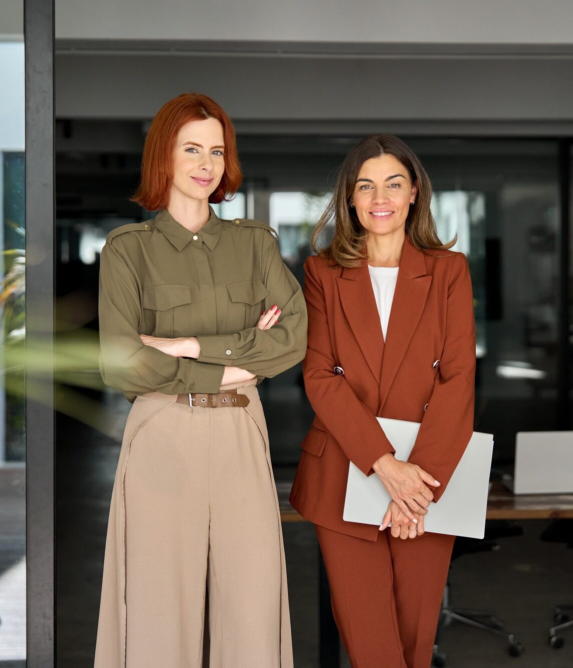 Portrait of two happy elegant business women standing at work in modern office.